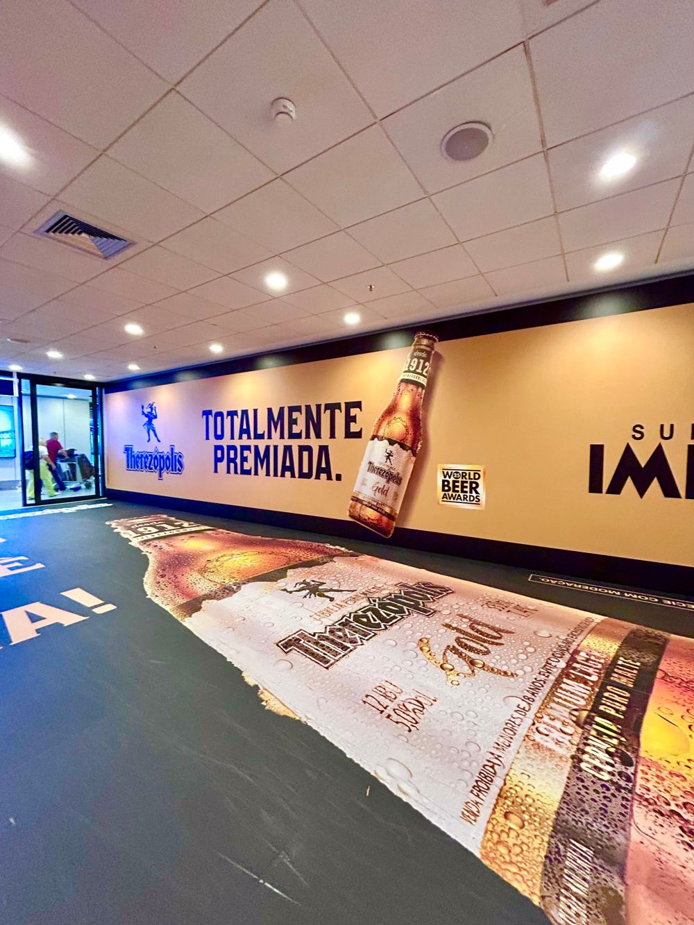 Campanha Totalmente Premiada da Therezópolis no aeroporto de Florianópolis, com garrafa gigante no chão e na parede