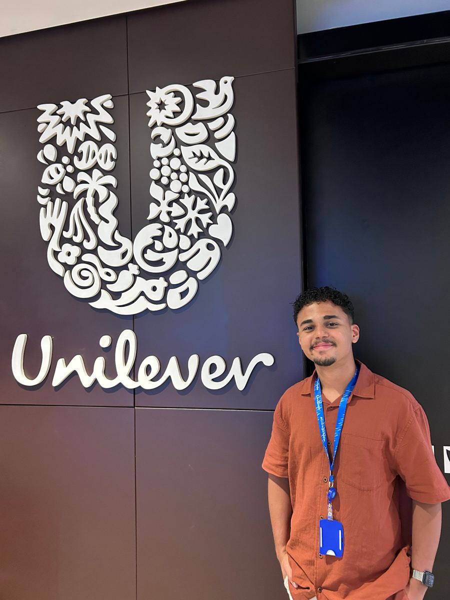 Amós sorrindo ao lado do logo da Unilever no escritório