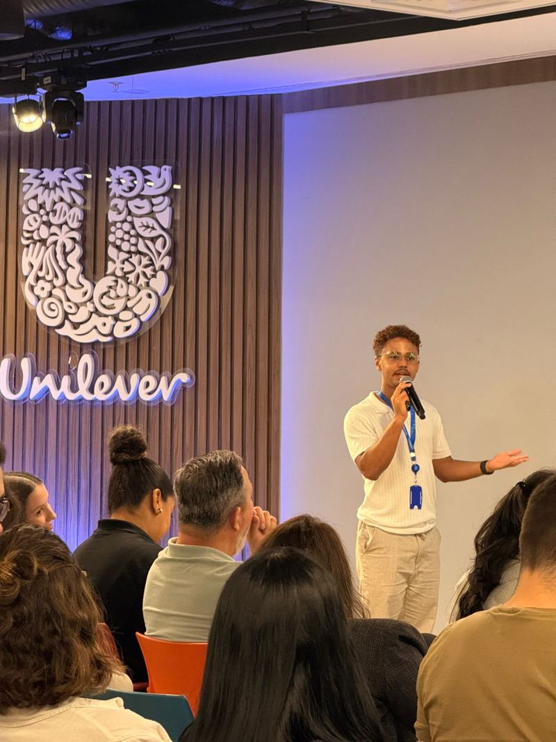 Amós falando ao microfone para o time no auditório da Unilever