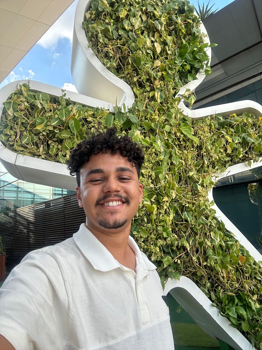 Selfie de Amós sorrindo em frente ao boneco da Vivo feito de plantas